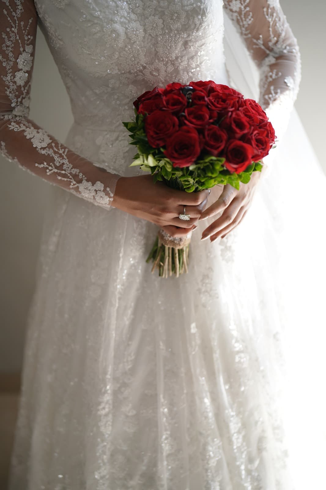 Red rose bouquet held against lace gown, ring detail visible