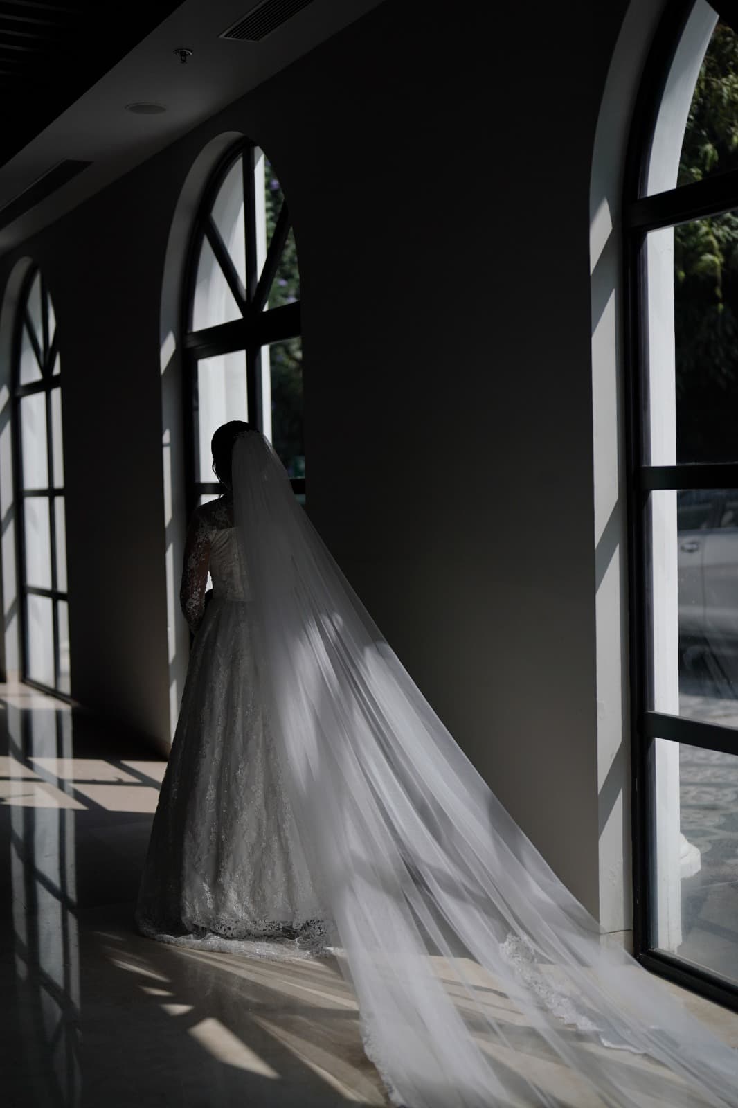 Cathedral veil flowing behind bride, dramatic arched windows